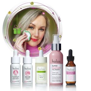 Sally uses a skincare product on her face from Sally's Well-ageing Bundle. In front of her is a collection of Holos Skincare products, including serums and creams in bottles and droppers. A gift box icon is featured in the upper left corner, curated by the Irish Beauty Fairy - Sally Foran